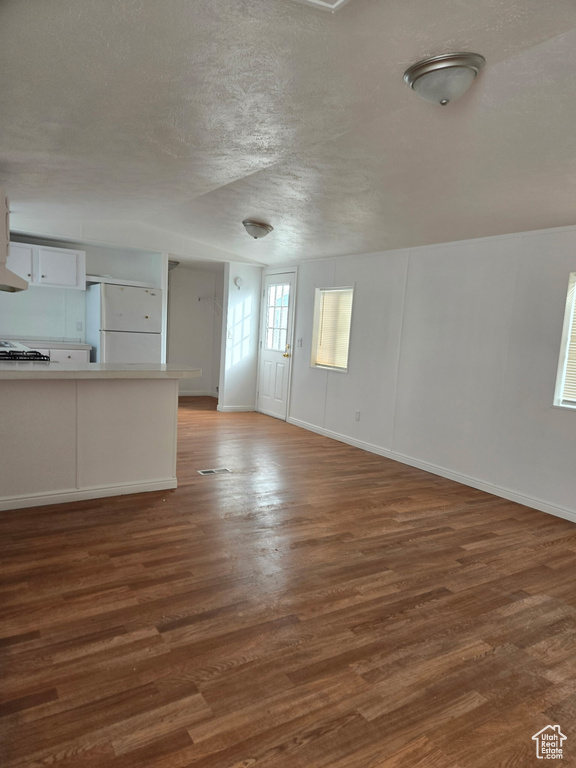 Unfurnished living room featuring dark wood finished floors, a textured ceiling, and baseboards