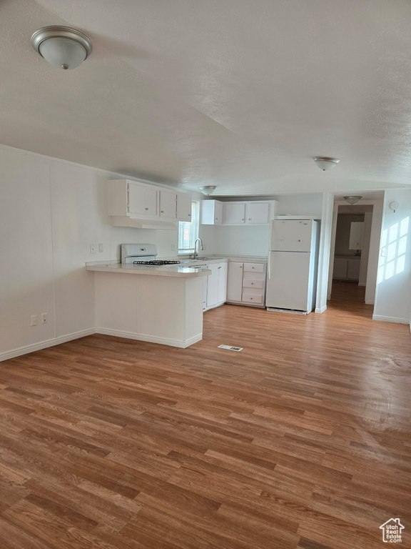 Kitchen with freestanding refrigerator, a sink, a peninsula, stove, and white cabinetry