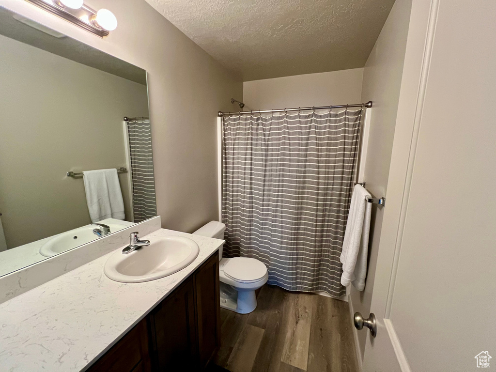 Full bath with wood finished floors, a textured ceiling, toilet, vanity, and a shower with curtain