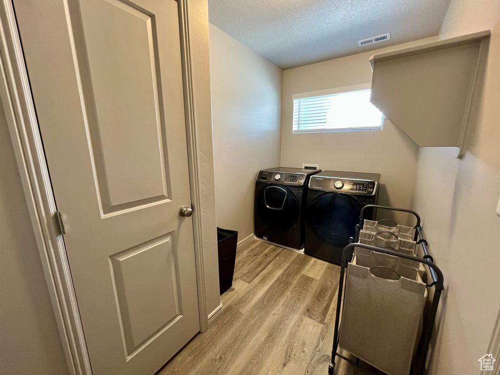 Washroom with independent washer and dryer, light wood-style floors, and a textured ceiling