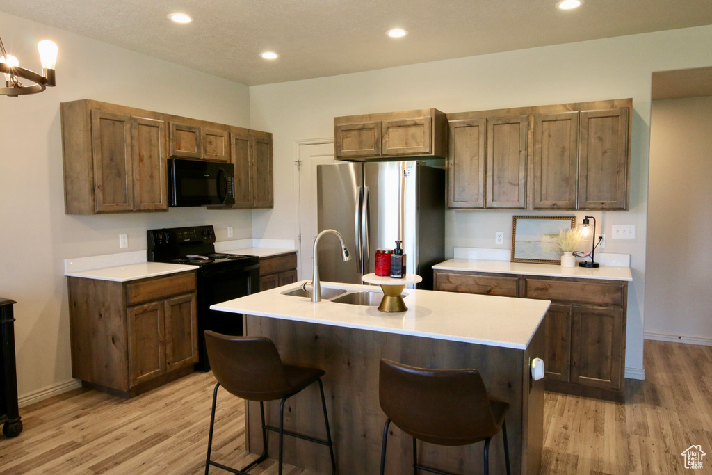 Kitchen featuring black appliances, a sink, light wood-type flooring, light countertops, and a kitchen bar