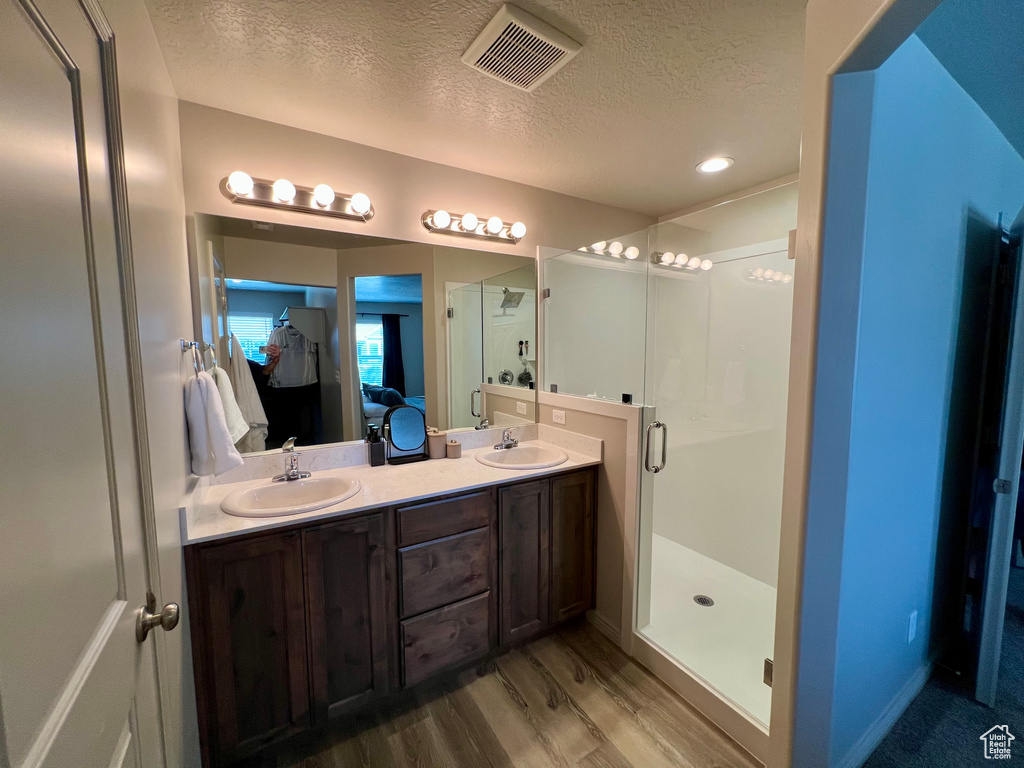 Ensuite bathroom with a textured ceiling, a stall shower, wood finished floors, double vanity, and recessed lighting