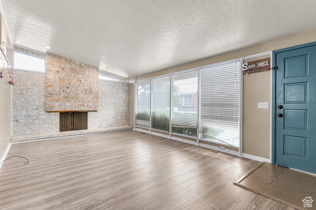 Unfurnished living room featuring a textured ceiling, healthy amount of natural light, wood finished floors, baseboards, and a fireplace
