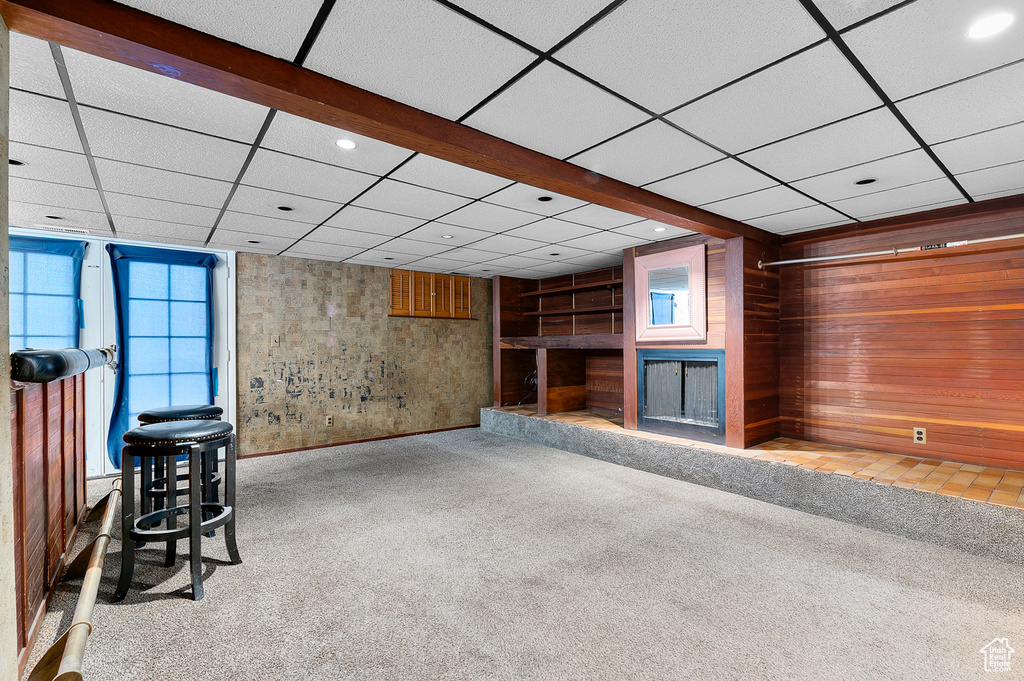 Unfurnished living room featuring carpet, a fireplace with raised hearth, plenty of natural light, a paneled ceiling, and recessed lighting