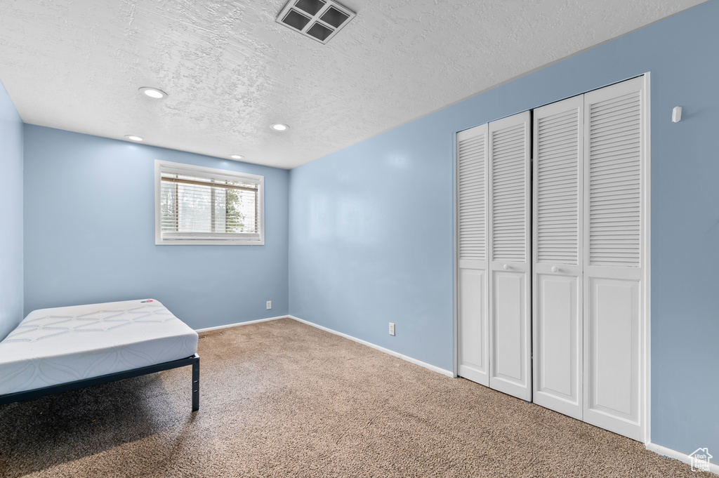 Unfurnished bedroom with carpet flooring, a textured ceiling, recessed lighting, a closet, and baseboards