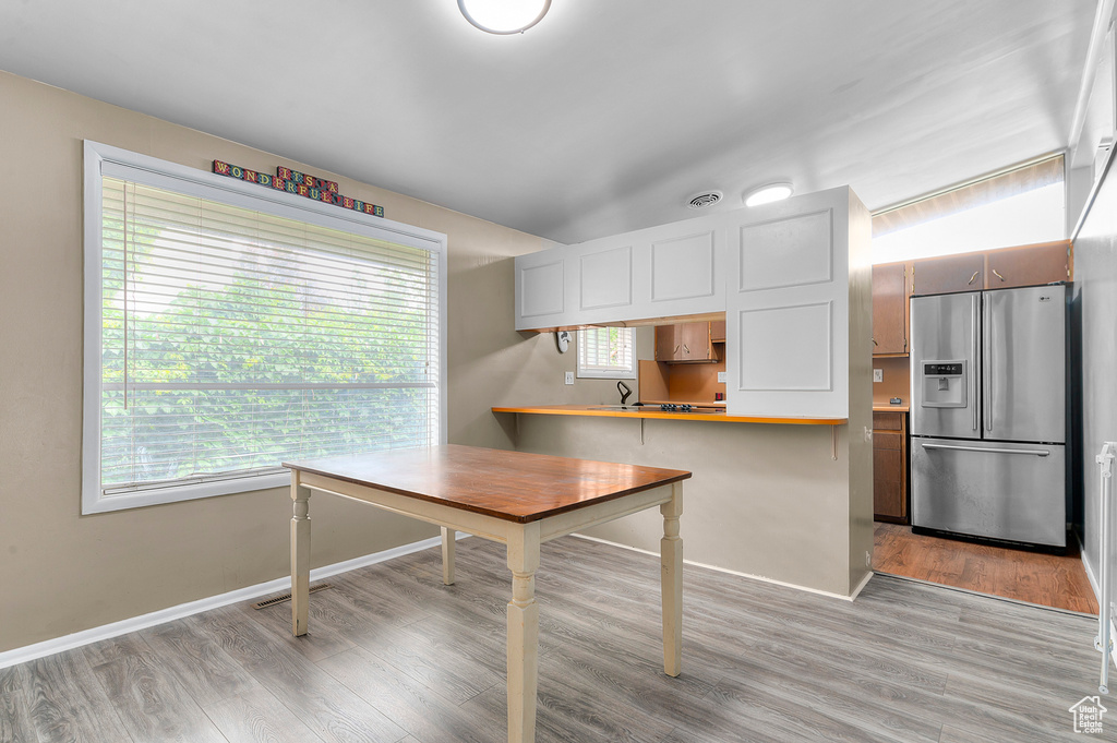 Kitchen with stainless steel refrigerator with ice dispenser, healthy amount of natural light, light wood-type flooring, and baseboards