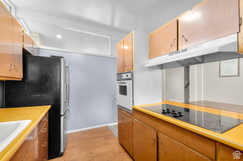 Kitchen featuring oven, under cabinet range hood, light countertops, light wood-type flooring, and black electric stovetop