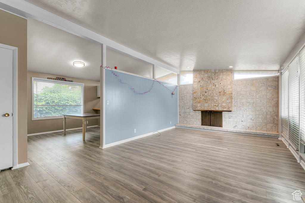 Unfurnished living room with baseboards, a stone fireplace, wood finished floors, and a textured ceiling