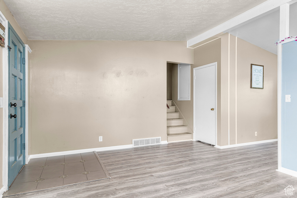 Unfurnished room with a textured ceiling, vaulted ceiling, wood finished floors, stairway, and baseboards