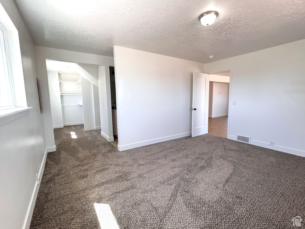 Empty room with carpet flooring, a textured ceiling, and baseboards