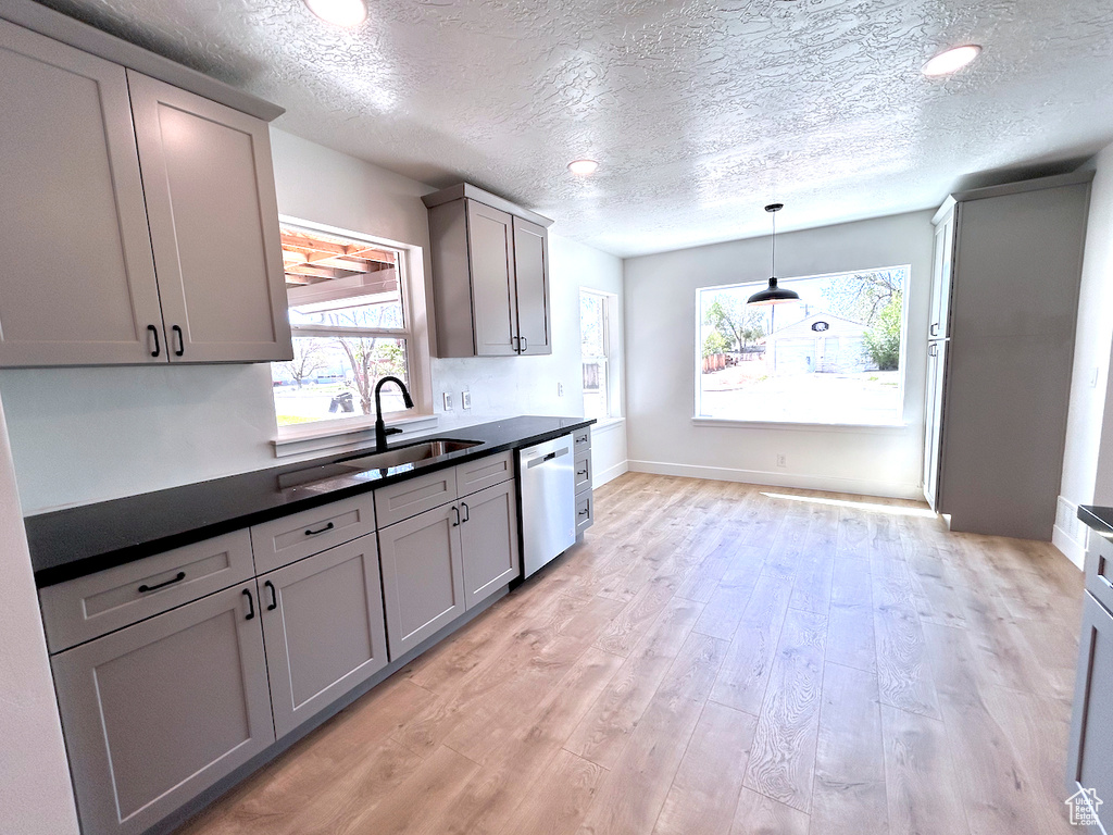 Kitchen with stainless steel dishwasher, a sink, dark countertops, a textured ceiling, and gray cabinetry