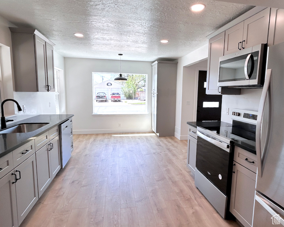 Kitchen featuring appliances with stainless steel finishes, a sink, dark countertops, a textured ceiling, and light wood-type flooring