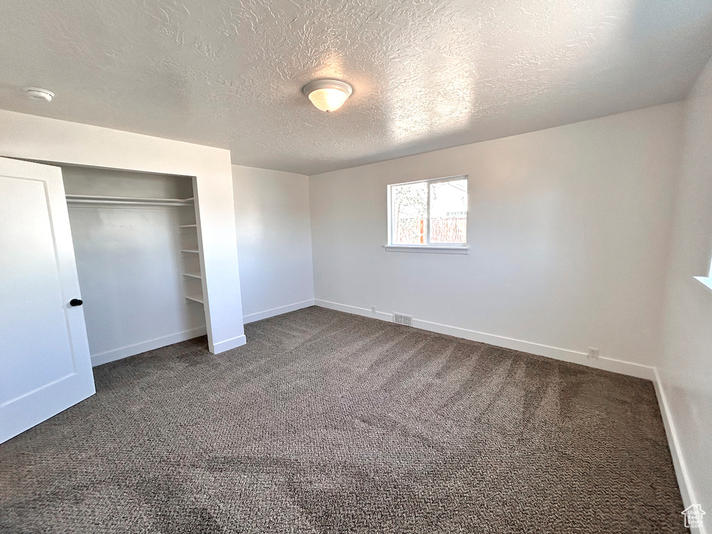 Unfurnished bedroom featuring baseboards, carpet flooring, a textured ceiling, and a closet