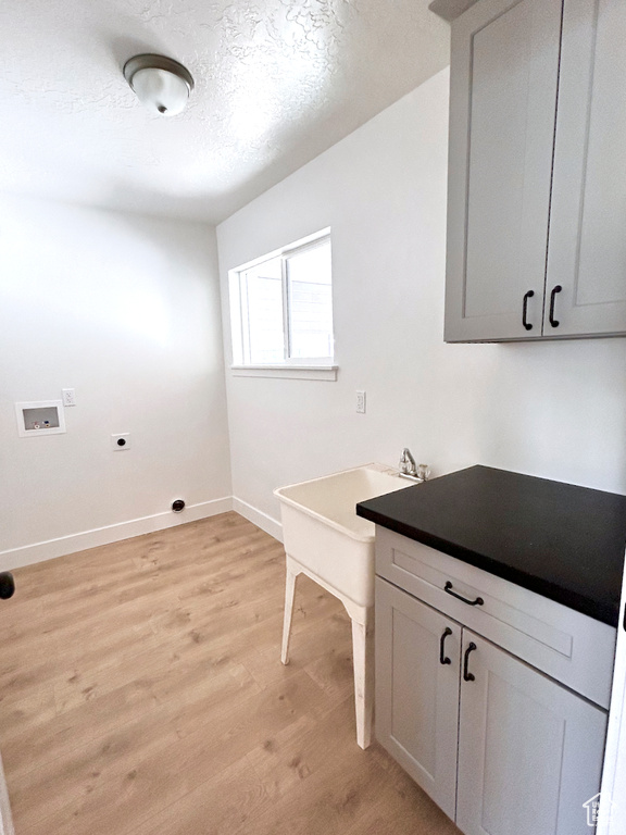 Washroom featuring electric dryer hookup, hookup for a washing machine, light wood finished floors, cabinet space, and a textured ceiling