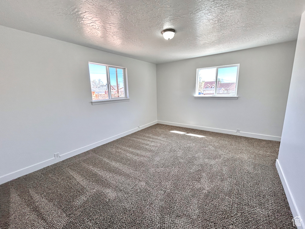Carpeted spare room featuring a textured ceiling and baseboards