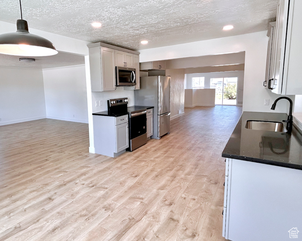 Kitchen featuring appliances with stainless steel finishes, a sink, open floor plan, light wood-style floors, and a textured ceiling