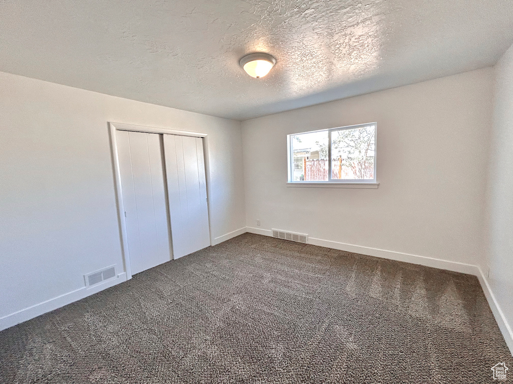 Unfurnished bedroom featuring a closet, dark carpet, baseboards, and a textured ceiling