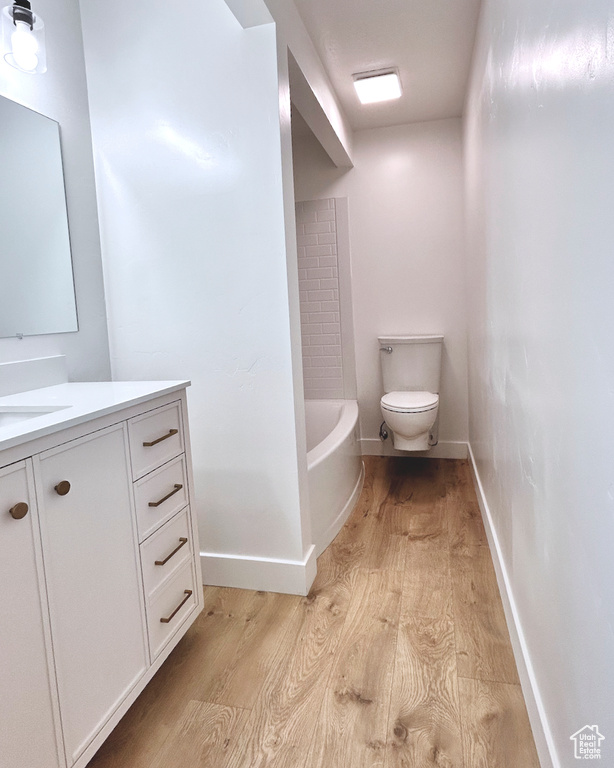 Full bathroom featuring wood finished floors, toilet, vanity, a tub, and baseboards