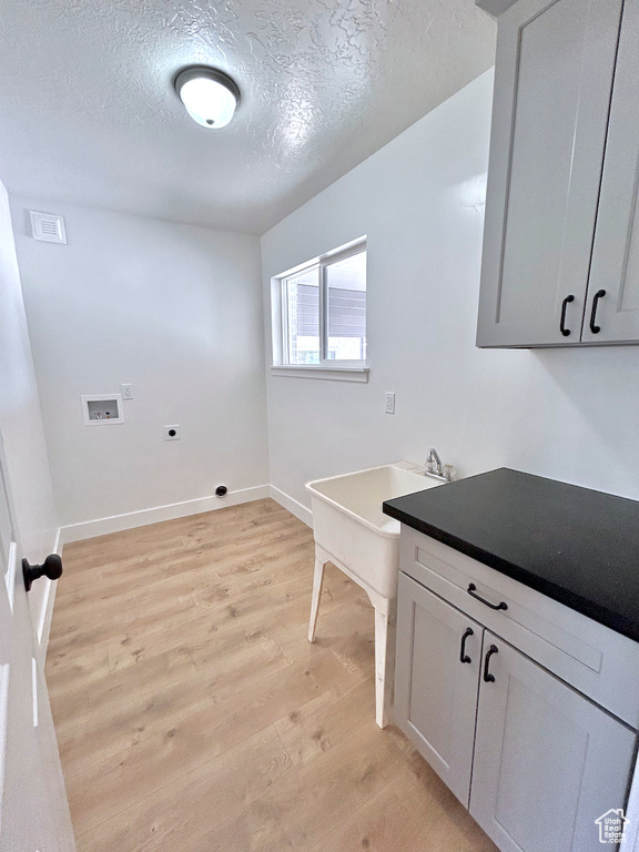 Laundry area featuring hookup for an electric dryer, washer hookup, light wood-style floors, a textured ceiling, and baseboards