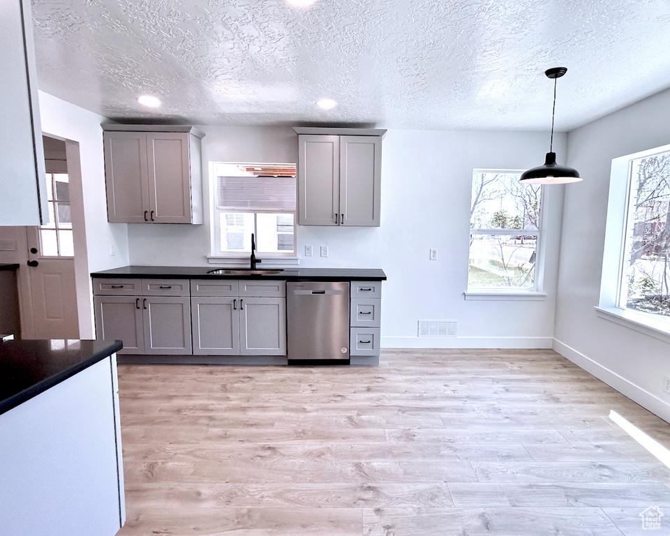 Kitchen featuring dishwasher, gray cabinetry, dark countertops, a textured ceiling, and light wood-style flooring