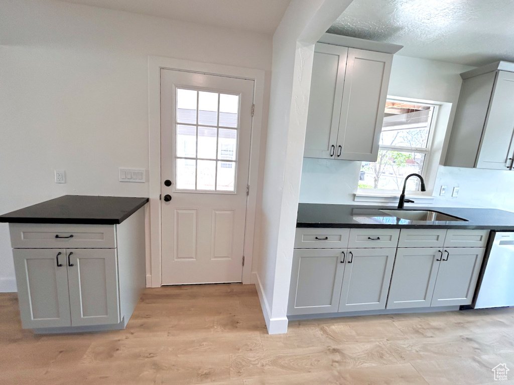 Kitchen featuring a sink, dishwashing machine, dark countertops, and light wood-style flooring