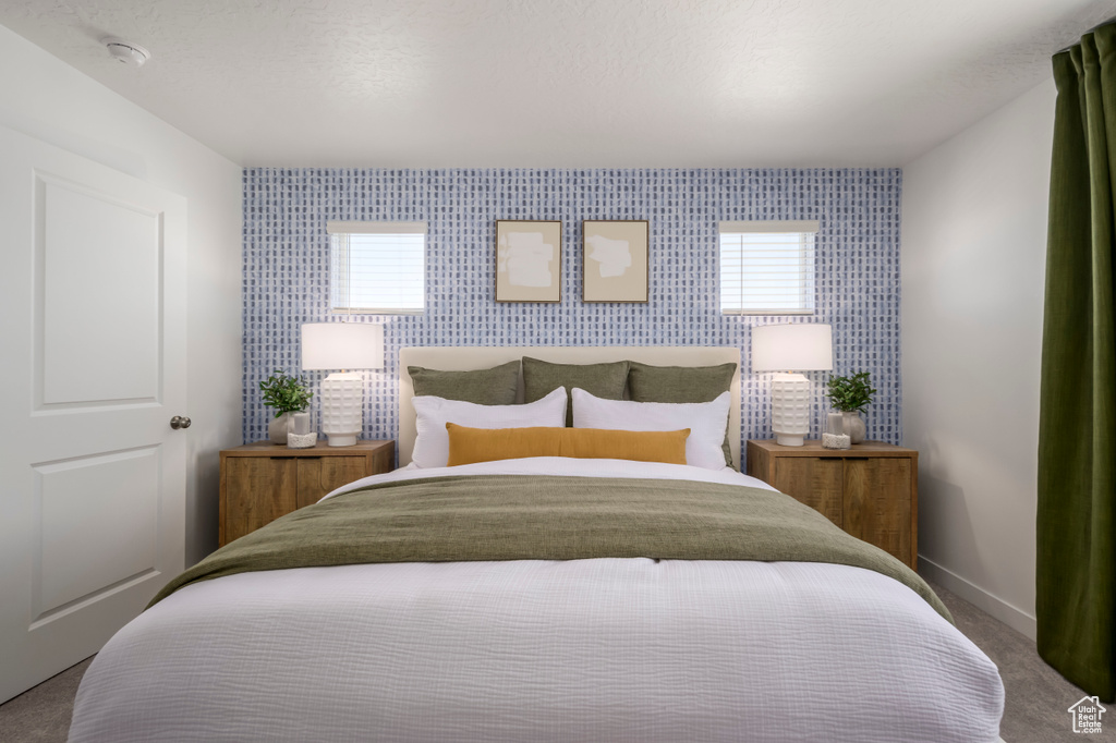 Bedroom featuring carpet flooring, wallpapered walls, baseboards, an accent wall, and multiple windows