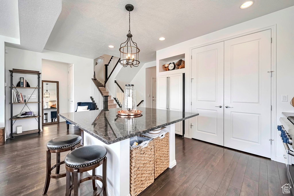 Kitchen featuring dark wood finished floors, a breakfast bar area, a textured ceiling, dark stone countertops, and recessed lighting