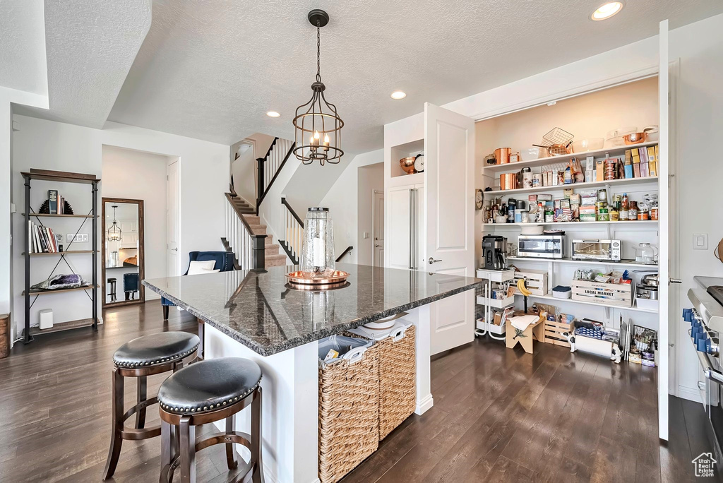 Kitchen with dark wood finished floors, a textured ceiling, a breakfast bar area, dark stone countertops, and recessed lighting