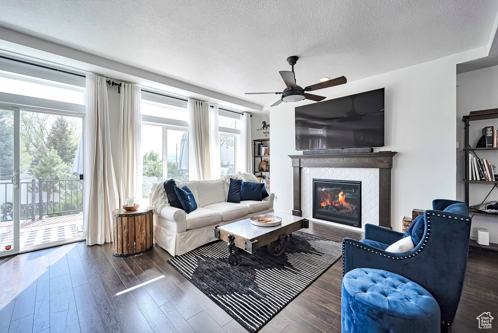 Living area featuring a textured ceiling, a glass covered fireplace, wood-type flooring, and ceiling fan
