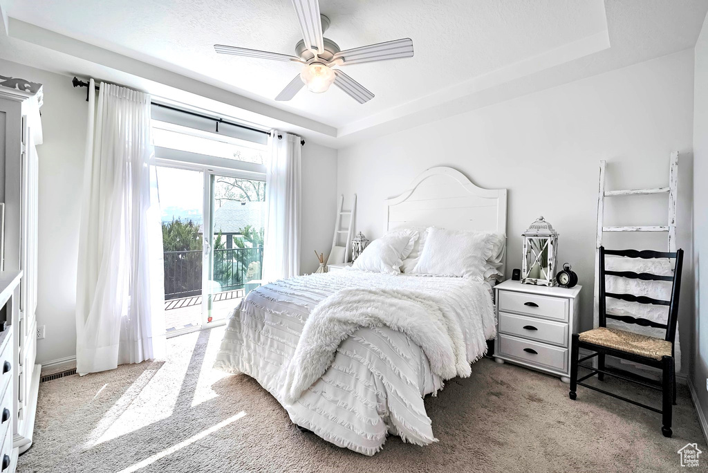 Carpeted bedroom featuring access to outside, a tray ceiling, and a ceiling fan