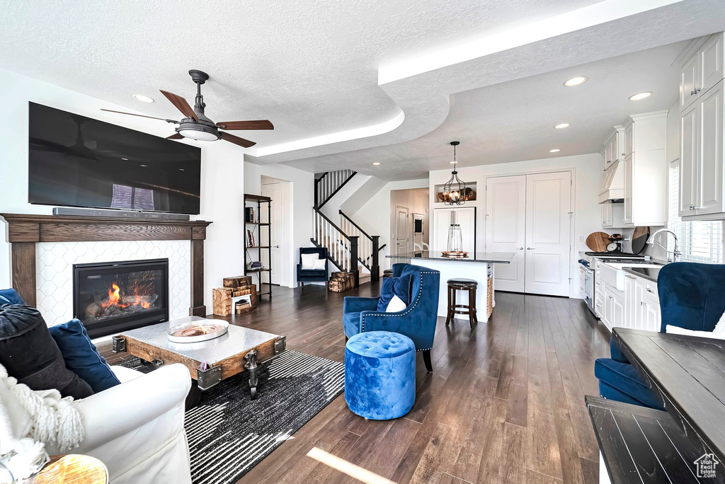 Living room with dark wood finished floors, a tile fireplace, a ceiling fan, a textured ceiling, and stairs