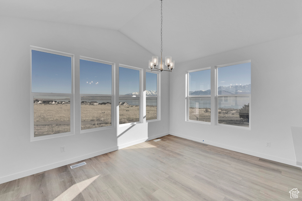 Empty room featuring a chandelier, light wood finished floors, lofted ceiling, and baseboards