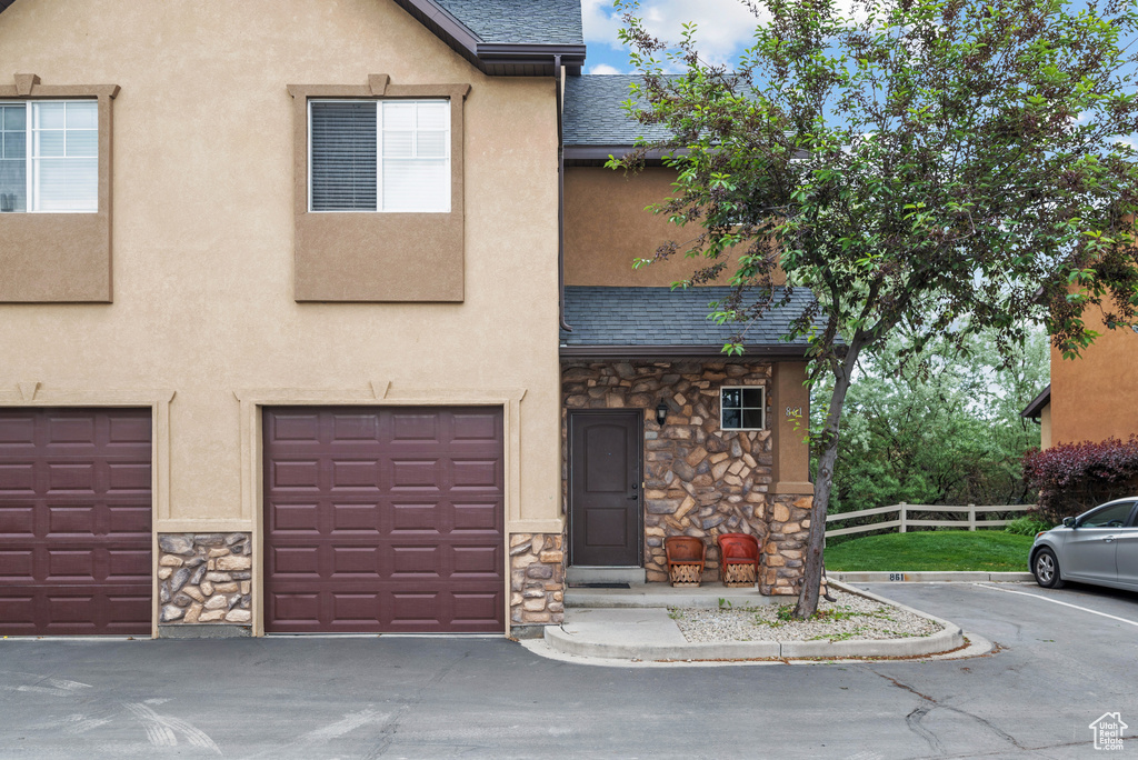 Townhome / multi-family property with stone siding, a shingled roof, stucco siding, and a garage