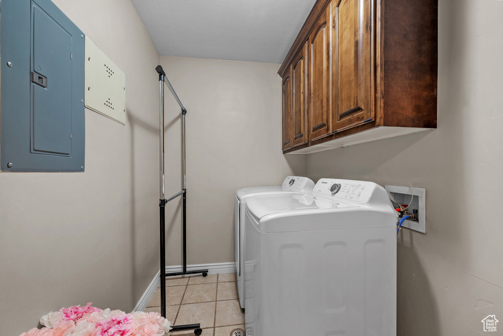 Washroom with electric panel, washer and dryer, light tile patterned floors, baseboards, and cabinet space