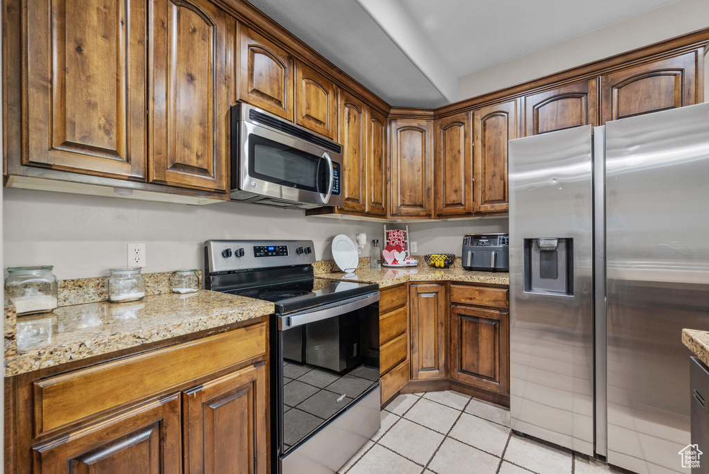 Kitchen with appliances with stainless steel finishes, light tile patterned floors, light stone countertops, and brown cabinets
