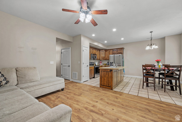 Living area with a chandelier, ceiling fan, recessed lighting, light wood-style floors, and baseboards