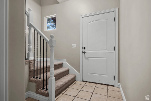 Entryway featuring baseboards, light tile patterned floors, and stairway