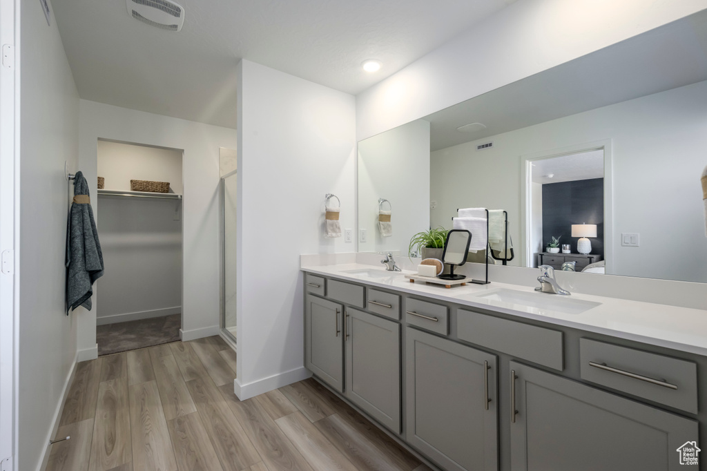 Ensuite bathroom with wood finished floors, double vanity, baseboards, a walk in shower, and a walk in closet