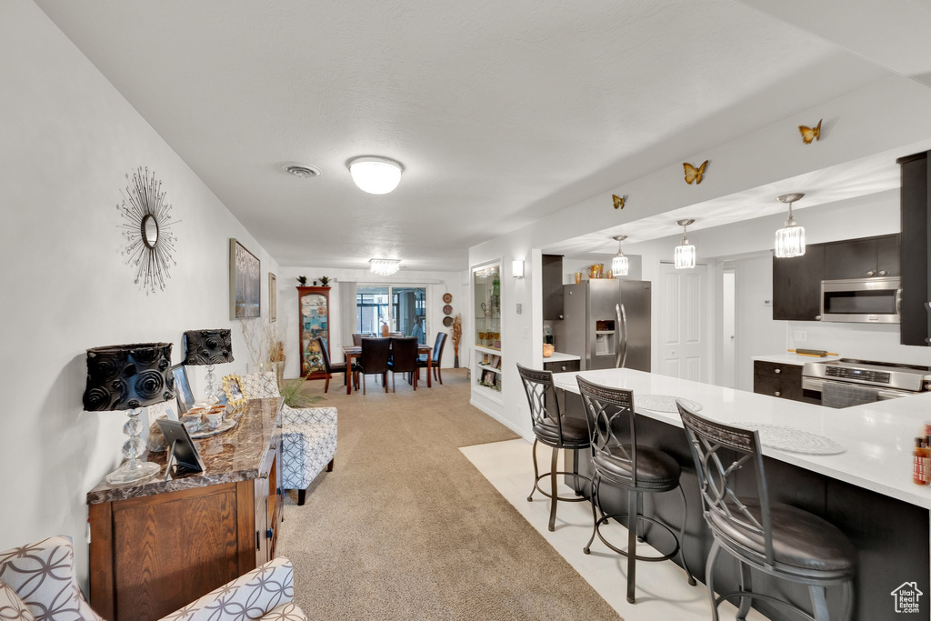 Kitchen with stainless steel appliances, a breakfast bar area, light countertops, light colored carpet, and pendant lighting