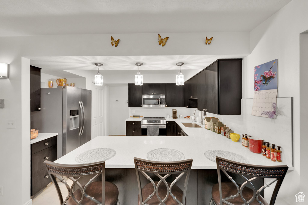 Kitchen featuring appliances with stainless steel finishes, light countertops, a peninsula, and a kitchen breakfast bar