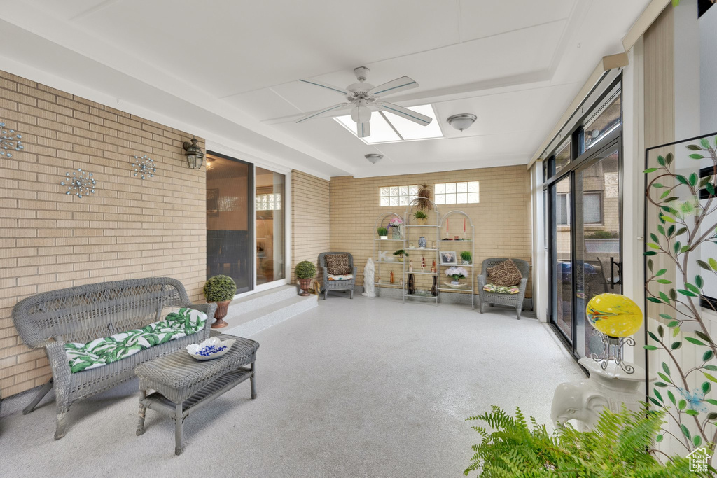 Sitting room with brick wall, a ceiling fan, a skylight, and speckle patterned floor
