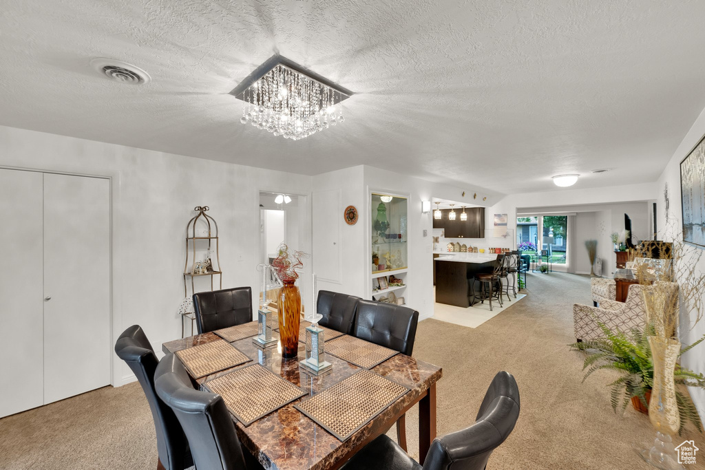 Dining area featuring light colored carpet, a chandelier, and a textured ceiling