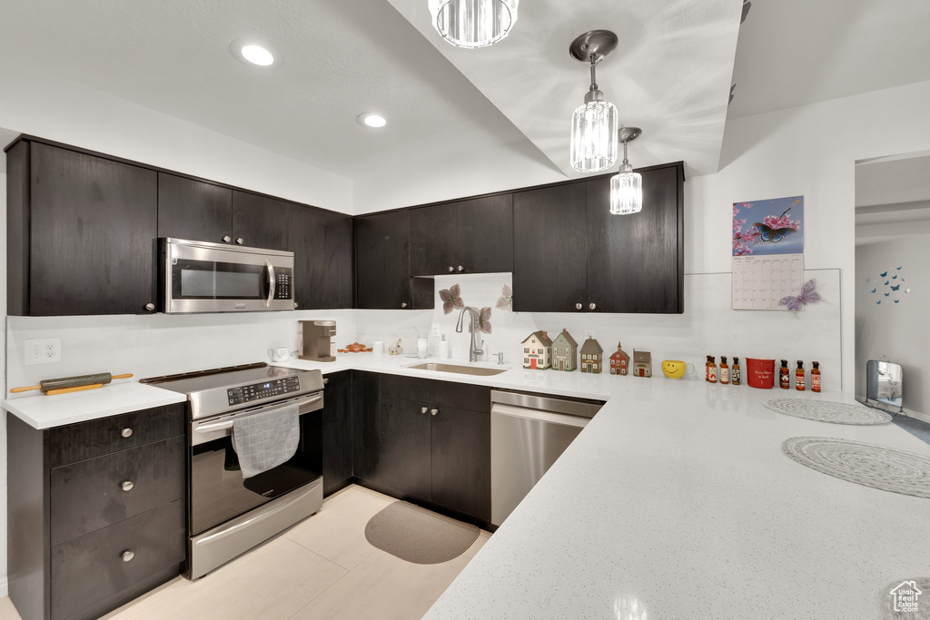 Kitchen featuring appliances with stainless steel finishes, a sink, light countertops, recessed lighting, and decorative light fixtures