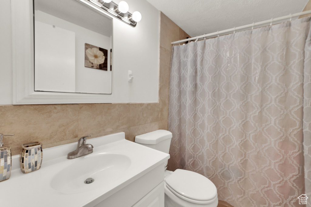 Full bathroom with toilet, vanity, decorative backsplash, and curtained shower