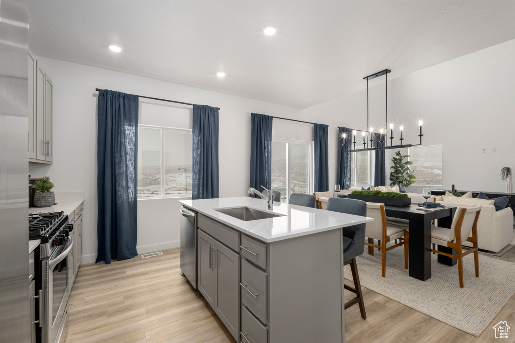 Kitchen featuring a sink, appliances with stainless steel finishes, gray cabinets, a breakfast bar area, and light wood finished floors