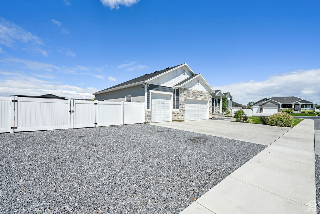 View of side of property with a gate, stone siding, a garage, concrete driveway, and board and batten siding