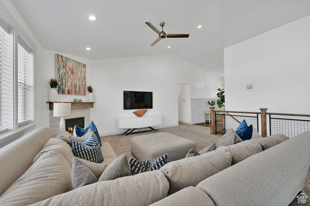 Living room with carpet flooring, a ceiling fan, vaulted ceiling, recessed lighting, and a warm lit fireplace
