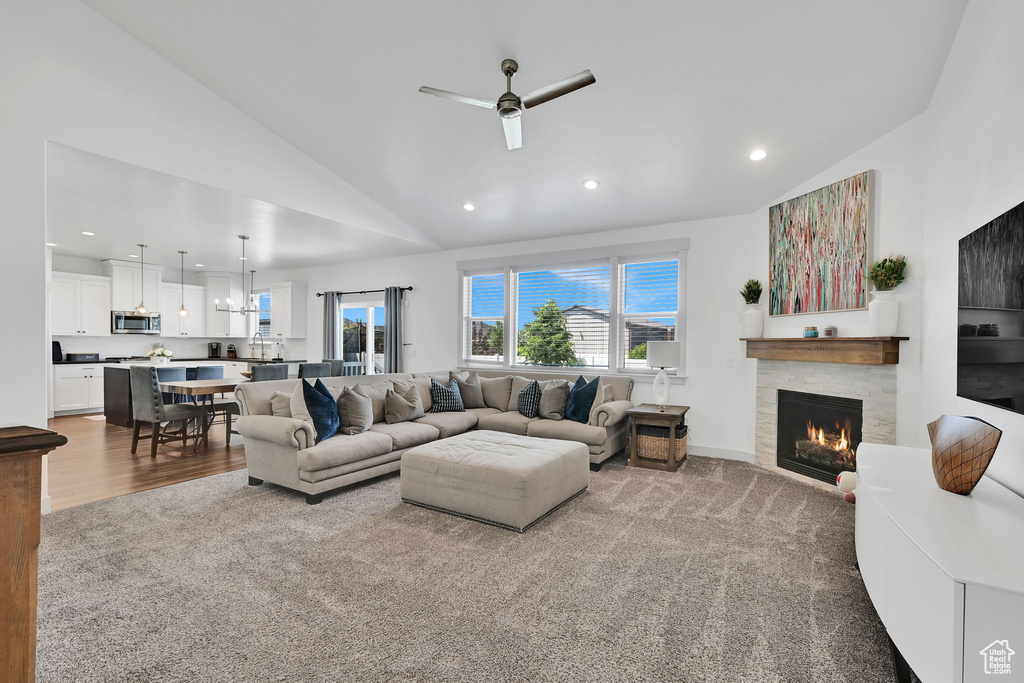 Carpeted living room featuring a ceiling fan, a stone fireplace, recessed lighting, high vaulted ceiling, and a sink