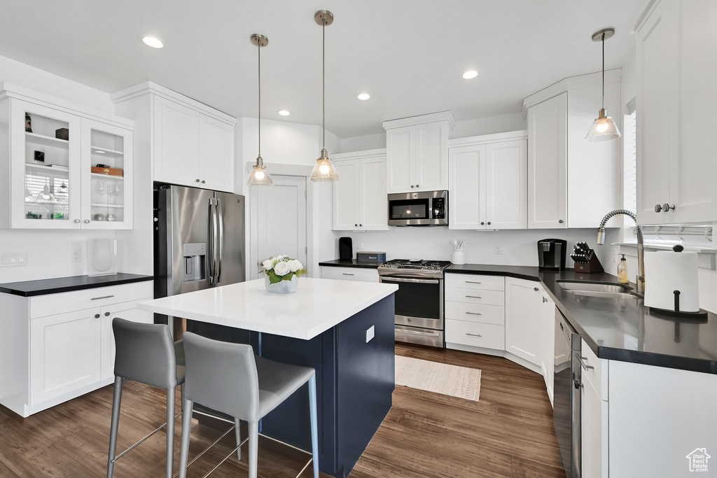 Kitchen featuring appliances with stainless steel finishes, dark countertops, a kitchen island, white cabinets, and dark wood-style flooring