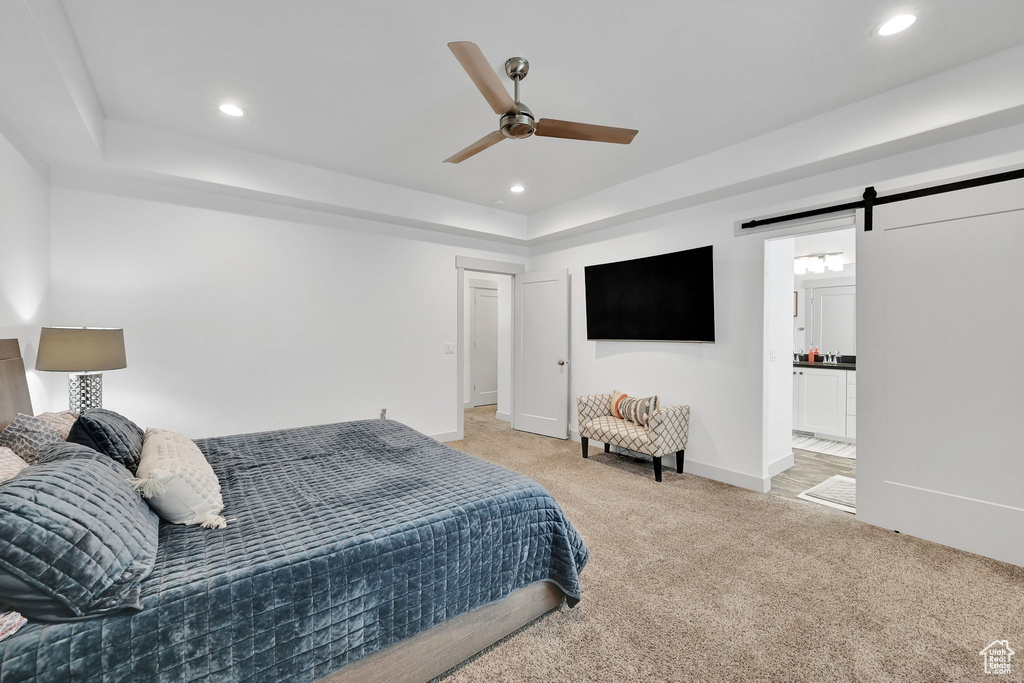 Bedroom with a barn door, light carpet, a raised ceiling, recessed lighting, and baseboards